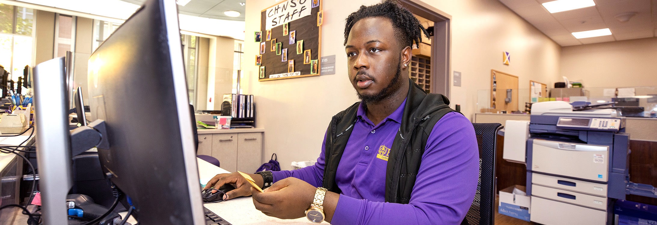 Man siting at computer in a purple shirt.